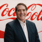 Hombre sonriente frente al logo Coca-Cola